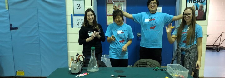 group of club members standing at demonstration table about fidget spinners
